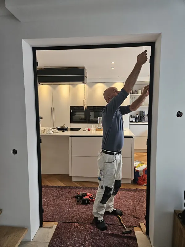 Handwerker von Wohntraum richtet eine neue Türzarge aus, im Hintergrund die renovierte Küche